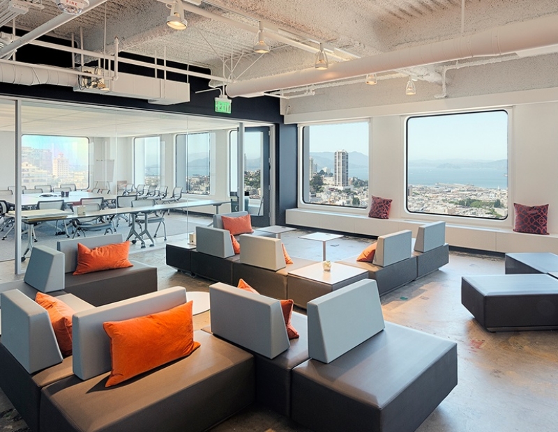 A modern office featuring couches and tables, offering a panoramic view of the city skyline through large windows. This is part of a 2025 office trend
