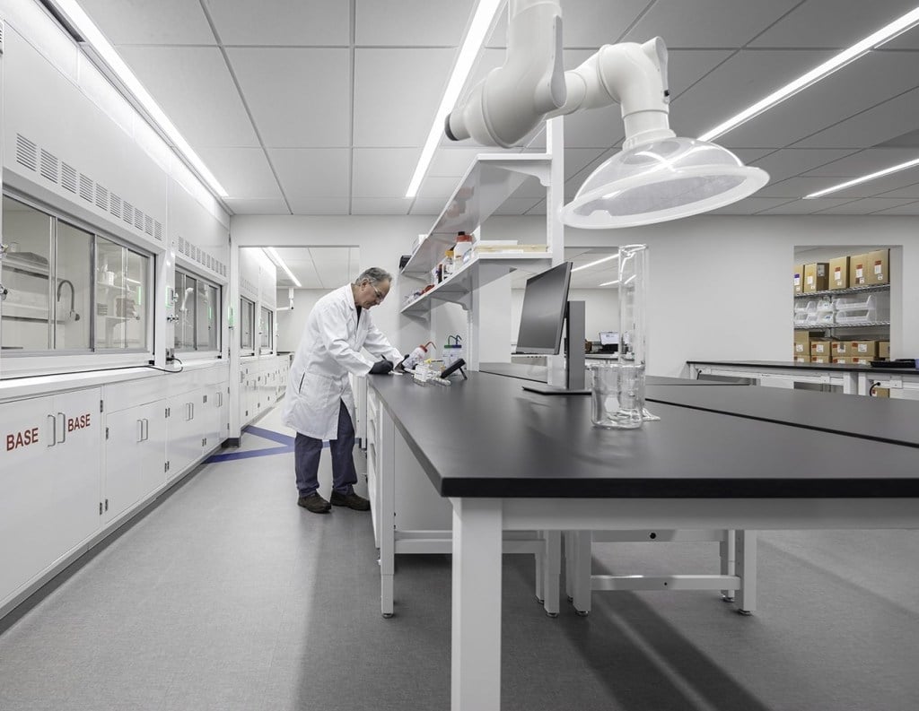 Scientist in a lab coat working at a bench in a modern, clean laboratory setting.