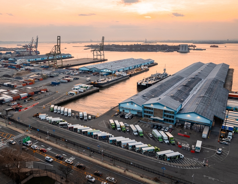 Aerial of Brooklyn Port Authority Piers showing cargo containers, trucks and ships with Governor's island and Statue of liberty in the background