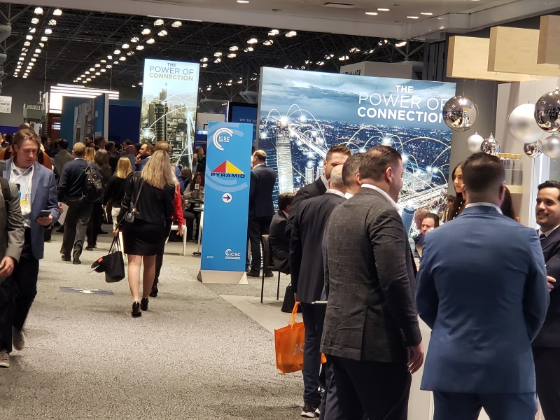 People standing at a booth and walking during ICSC tradeshow at Javits Center in New York City