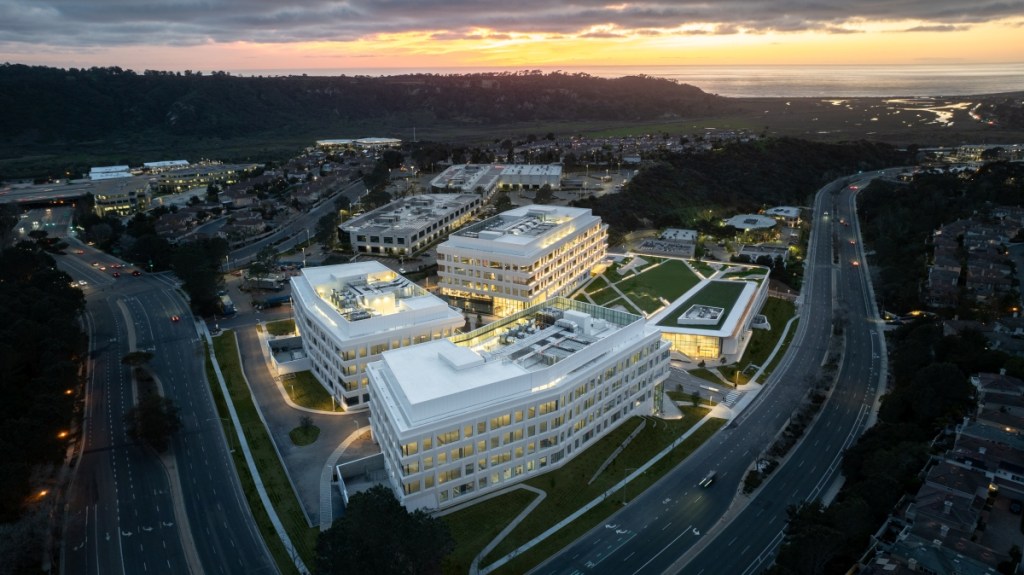 Aerial view of a modern building illuminated by the warm hues of sunset, showcasing its architectural design and surroundings.