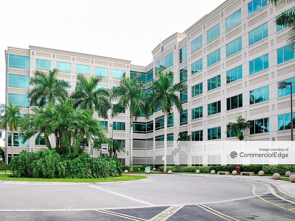 Exterior shot of Sawgrass Lake Center in Sunrise, Fla., a six-story building with glass and white concrete façade, surrounded by palm trees.