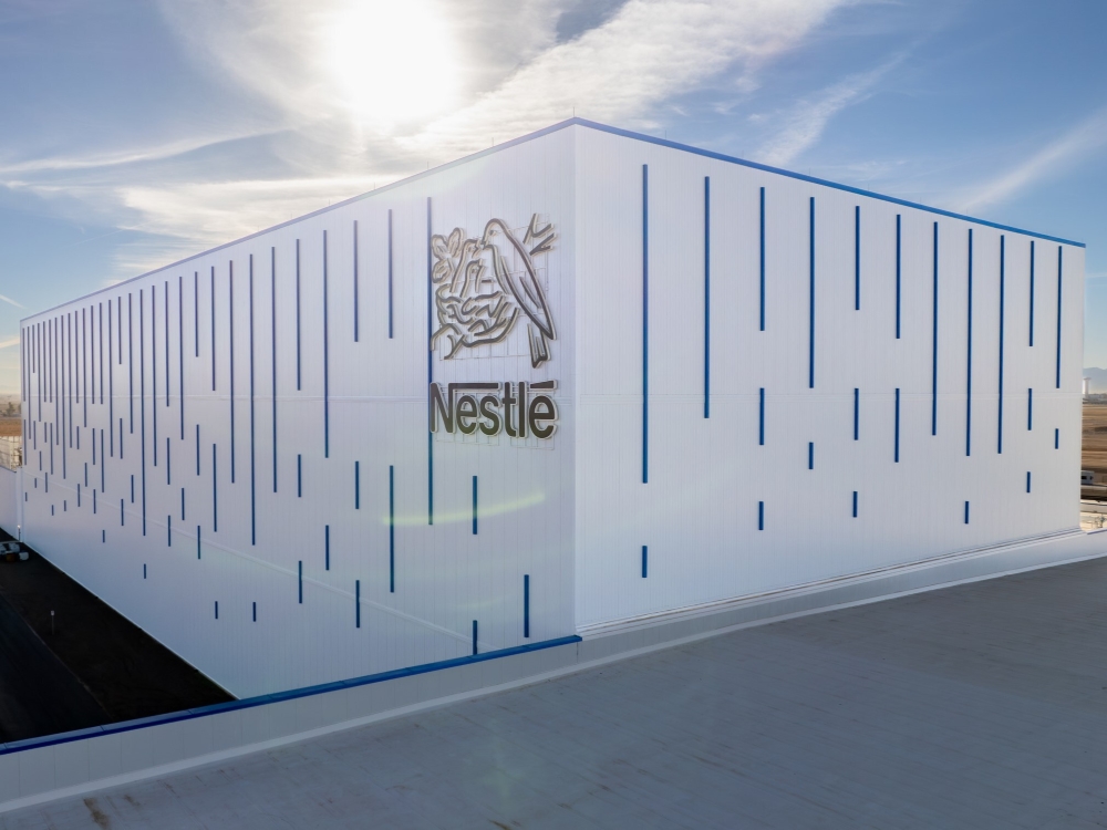 Exterior shot of Nestlé’s facility, a white one-story factory with blue lines. The building also features the company’s logo.