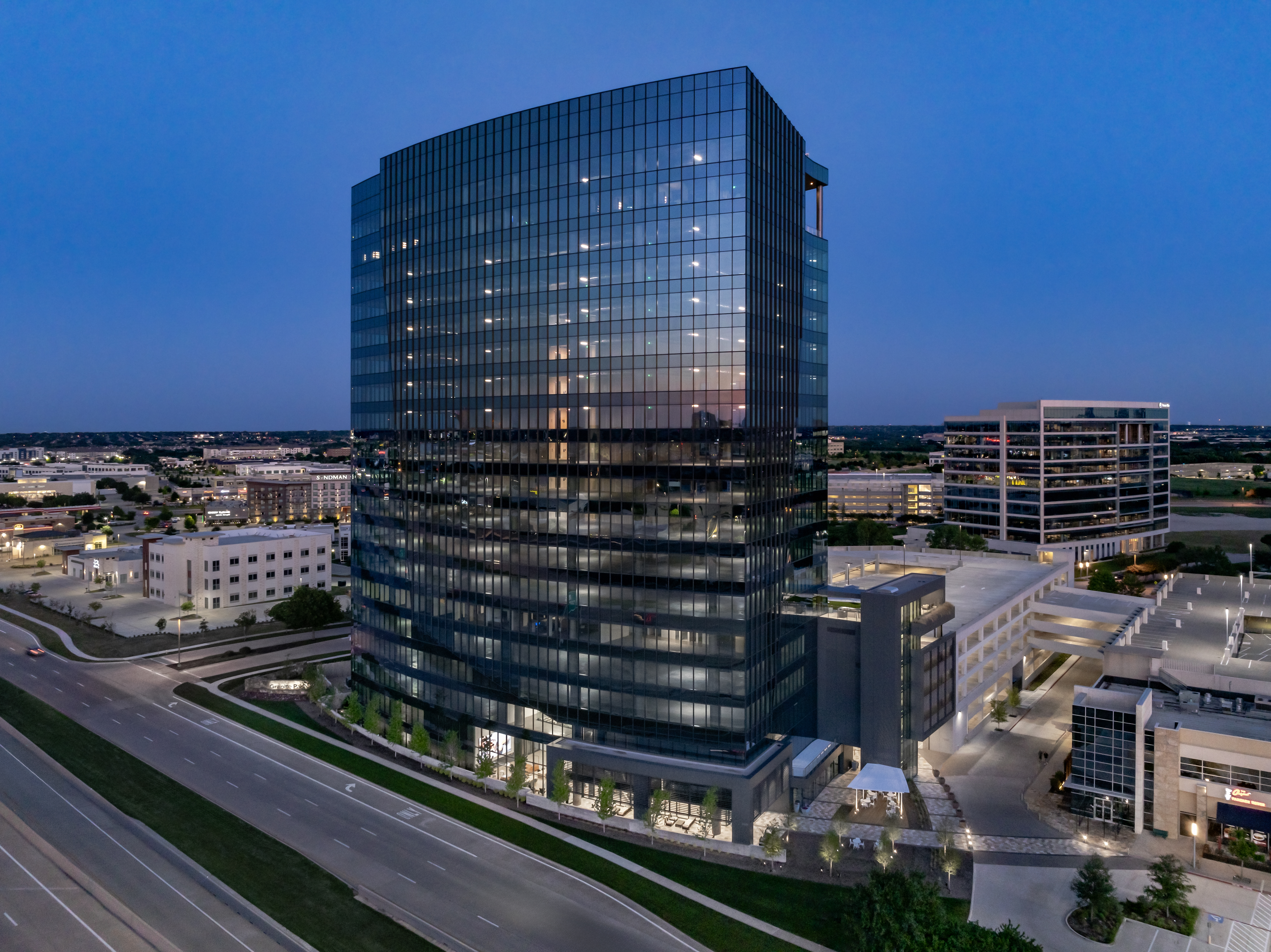 Aerial shot of Granite Park Six, a 19-story 422,109-square-foot office building in Plano, Texas. The image features the building overlooking Texas State Highway 121, at night.