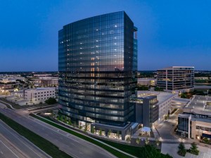 Aerial shot of Granite Park Six, a 19-story 422,109-square-foot office building in Plano, Texas. The image features the building overlooking Texas State Highway 121, at night.