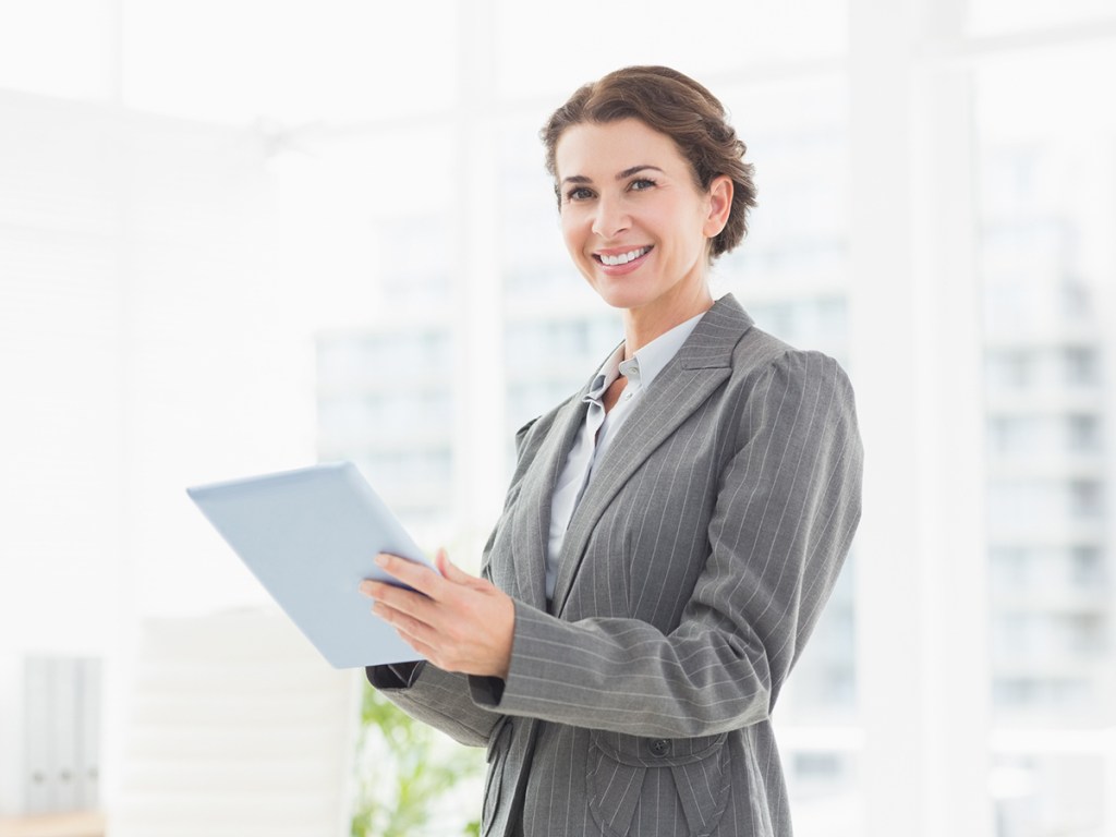 Smiling businesswoman looking at camera and using her tablet in an office